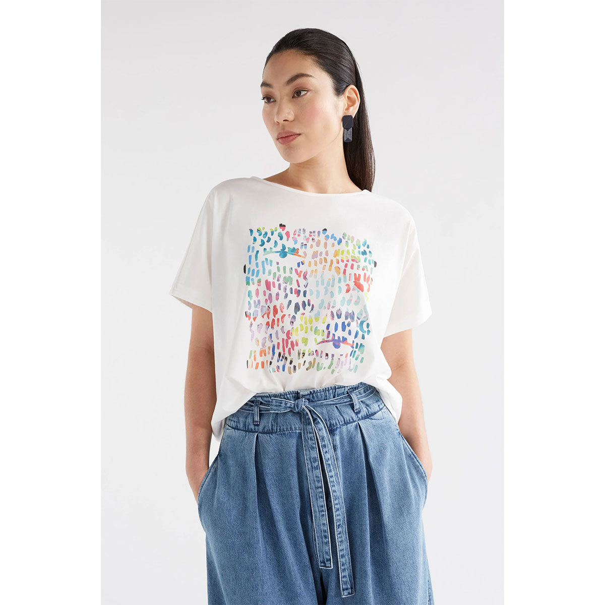 Front view of a model wearing a white tshirt with a colourful print with jeans.