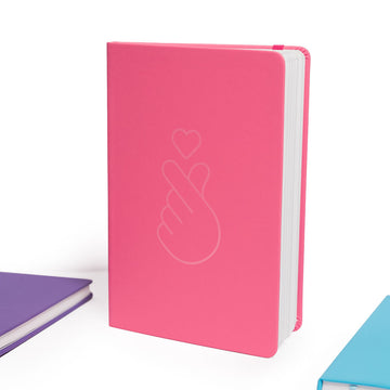 Pink notebook with a white outline of a hand making a heart and a heart symbol on a white background.