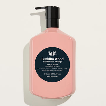 A pink pump bottle with a dark blue round label on the front with the text 'Budda Wood Hand Balm'.