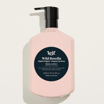 A pale pink bottle with a black pump lid and a dark teal circle in the middle. The text 'Leif Wild Rosella Alpine Pepper Damascan Rose Body Lotion' is visible in white in the circle along with further product information.