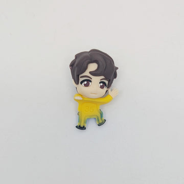 Small figurine of a character with dark hair and a yellow outfit on a light gray background.