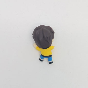 Small figurine of a character with dark hair and a yellow outfit on a light gray background.