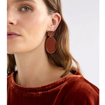 An image of a pair of earrings in a glossy enamel Spice coloured finish with a large oval drop from a smaller square stud.