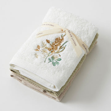 Three face washes folded and tied together. The top one is white with an embroidered wattle flower.