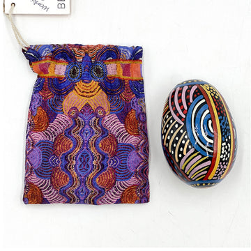 An ornamental egg next printed with artwork by Nora Nyutjanka Davidson next to a matching fabric sleeve.