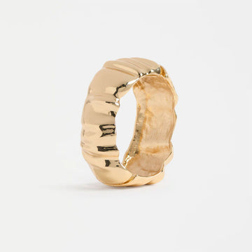 Gold bangle with a textured design on a light gray background.