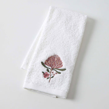 A white hand towel folded over embroidered with a flower.