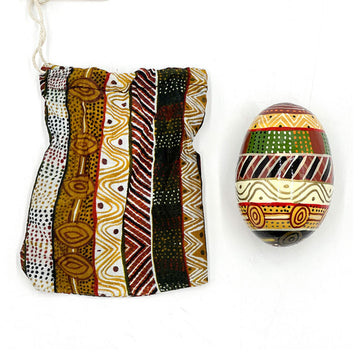 An ornamental egg printed with artwork by Josette Papajua next to a matching fabric sleeve.