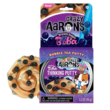 An open card packet titled 'Crazy Aarons Brown Sugar Boba Bubble Tea Putty' with a round container of putty inside the box. There is some light brown putty with black boba pieces next to the box.