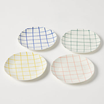 Four white ceramic plates with grid patterns in blue, green, yellow, and red on a white background.
