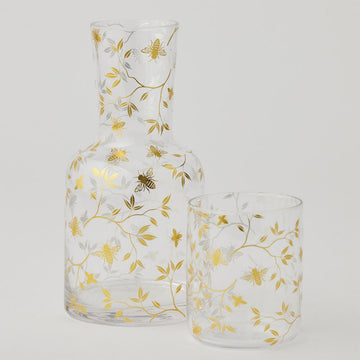 A carafe and glass with gold bee and leaf pattern on a white background.