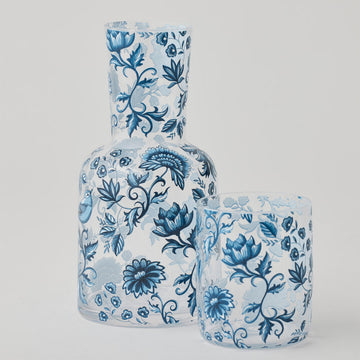 Set of glass carafe and tumbler with blue floral patterns on a gray background.