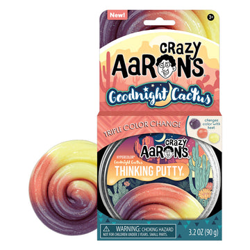 An open card packet titled 'Crazy Aarons Goodnight Cactus' with a round tub of putty inside. There is some putty next to the box with three different colours.