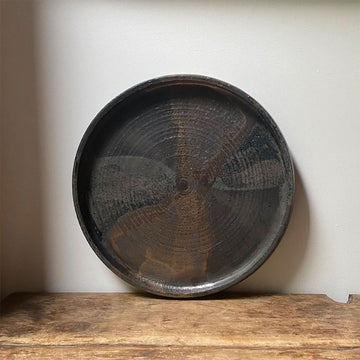 Round dark ceramic tray on a wooden surface with a light background.