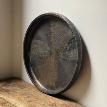 Round dark ceramic tray on a wooden surface with a light background.