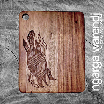 Wooden cutting board with laser-cut design on a gray stone surface, featuring the brand 'ngarga warendj'.