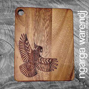 Wooden cutting board with an engraved cockatoo design on a gray surface, branded 'ngarga warendj'.