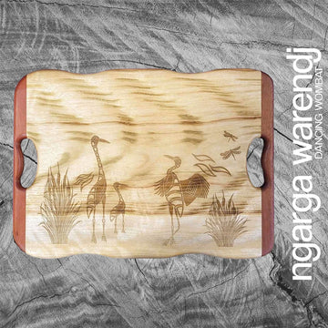 Wooden cutting board with engraved design of birds on a gray surface, featuring the brand 'ngarga warendj'.
