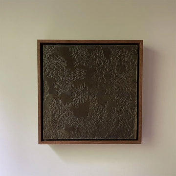 Textured wall art in a wooden frame on a plain wall.