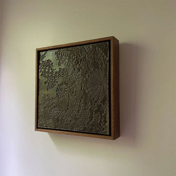 Textured wall art in a wooden frame on a plain wall.