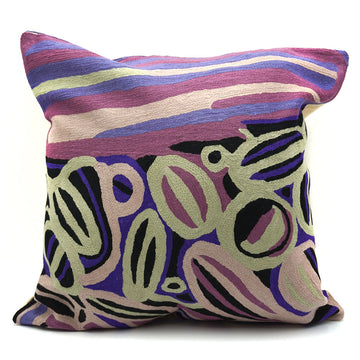 A square cushion made from wool and printed with artwork by Anmanari Brown in purple, cream and blue.