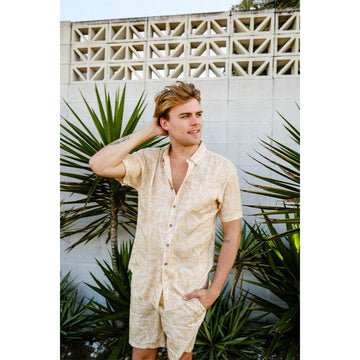 Front view of a man wearing a matching short sleeve shirt and shorts in a light cream colour subtly printed with palm leaves.