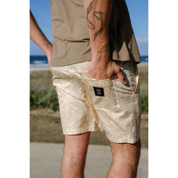 Front view of a man wearing a matching short sleeve shirt and shorts in a light cream colour subtly printed with palm leaves.