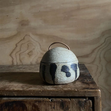 Small ceramic pot with a handle on a wooden surface against a wooden background.