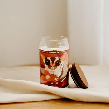 A candle in a can shaped container with an illustration of a sugar glider on the front