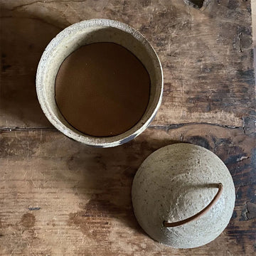 Small ceramic pot with a handle on a wooden surface against a wooden background.