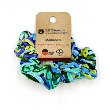A scrunchie printed with artwork by Cedric Varcoe in blue and green with a brown product label attached.