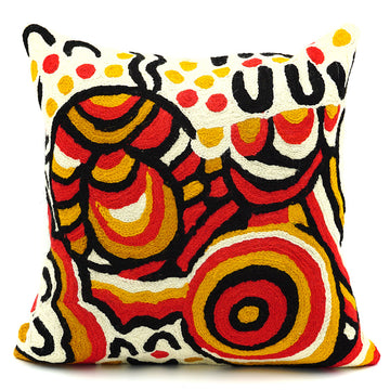 A square cushion made from wool and printed with artwork by Jeannie Uluru in red, orange, black and cream.