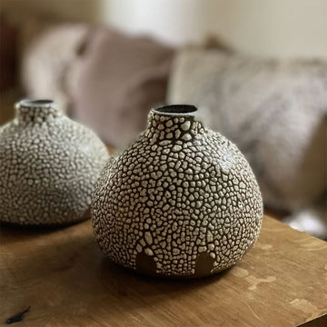 A small speckled ceramic vase on a wooden surface.