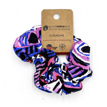 A scrunchie printed with artwork by Murdie Morris in purple and blue with a brown product label attached.