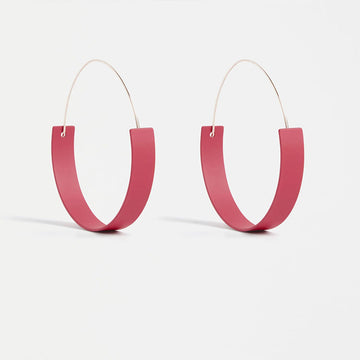 A pair of hooped earrings with a round flat bottom in a coral colour.
