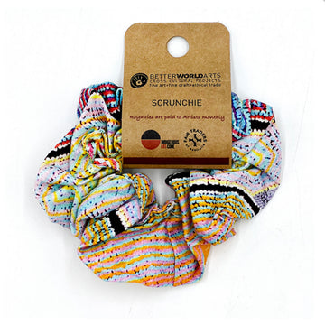 A scrunchie printed with artwork by Liddy Walker in a colourful pattern with a brown product label attached.