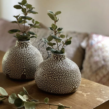 A small speckled ceramic vase on a wooden surface.