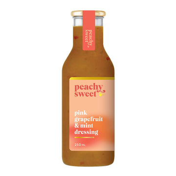 A bottle filled with dark yellow coloured dressing and a label on the front with the text 'Peachy Sweet Pink Grapefruit and Mint Dressing'.