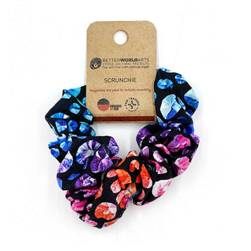 A scrunchie printed with artwork by Olivia Wilson with coloured spots on a black background and a brown product label attached.
