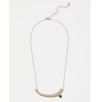 Gold necklace with a small black round pendant on a light grey background.