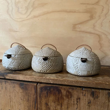 Three textured ceramic containers with lids on a wooden surface against a wooden background.