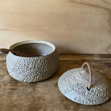 Three textured ceramic containers with lids on a wooden surface against a wooden background.