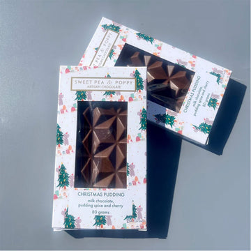 Two packages of Sweet Pea & Poppy Christmas pudding milk chocolate on a gray surface.