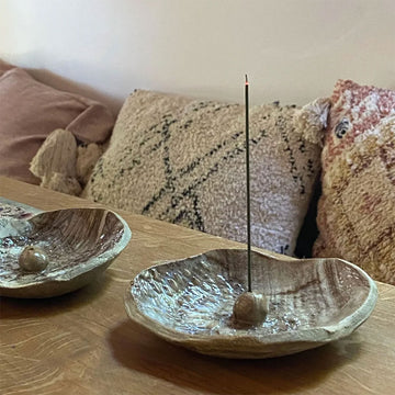 Two ceramic bowls with incense sticks on a wooden surface, with a textured pillow in the background.
