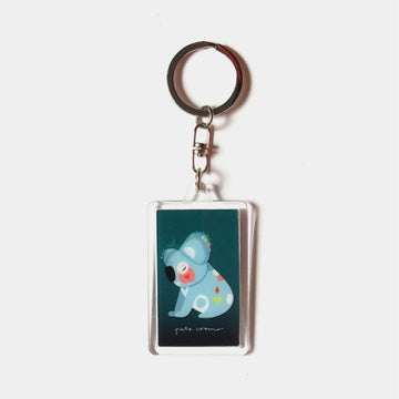 A rectangle keyring with a moving image of a koaal flying against a dark blue background.