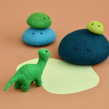 A green brontosaurus made from felt surrounded by green and blue felt rocks in different sizes.