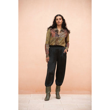 Person wearing a First Nations patterned shirt, black pants, and green boots against a peach wall.