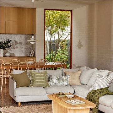 A square cushion in green with horizontal white stripes and a fringe edge on the left and right.