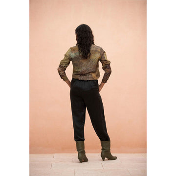 Person wearing a First Nations patterned shirt, black pants, and green boots against a peach wall.