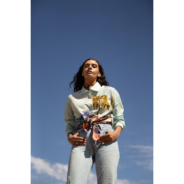 Woman standing against a clear blue sky wearing a light-colored shirt with a floral pattern.